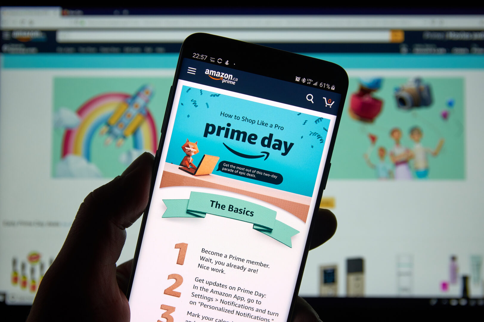 Image of a person holding a smartphone with Amazon Prime open in front of a computer screen on which Amazon is also open
