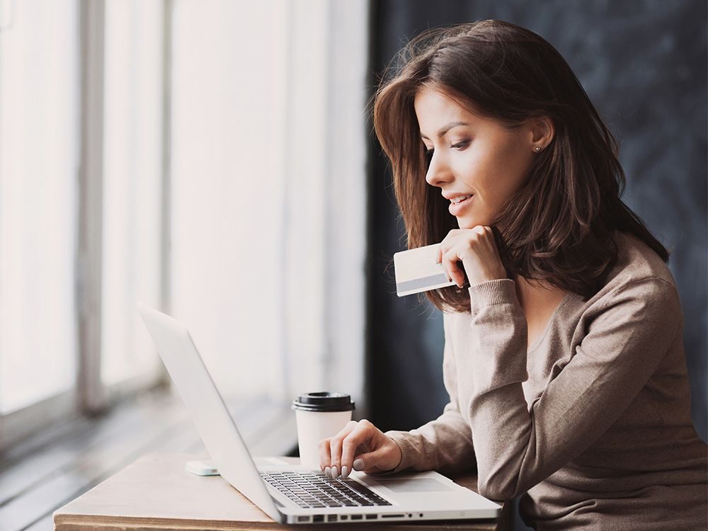 Focused woman using a laptop while holding a credit card, potentially engaging in online shopping or digital payment.